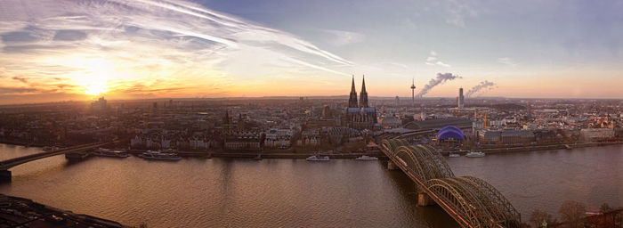 Panoramic view of hohenzollern bridge over rhine river by cityscape against sky during sunset