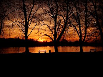 Silhouette bare trees by lake against sky during sunset