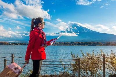 Young woman with luggage standing by lake kawaguchi holding map