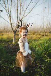 Portrait of cute girl in deer costume standing on grassy field against sky at park during halloween