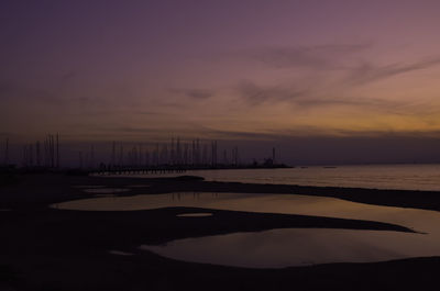 Scene in beach after rain with silhouettes of sails and a chapel at purple sunset