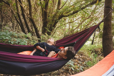 A man and a young kid lying in a hammock in the forest
