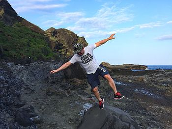 Full length of man on rock in sea against sky