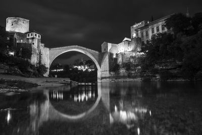 Arch bridge over river against buildings at night