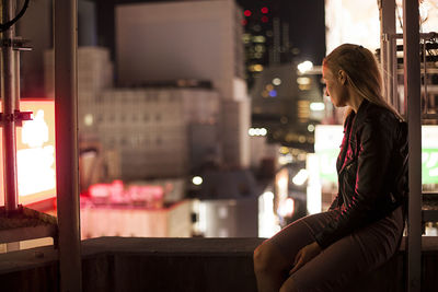 Side view of woman sitting in city at night