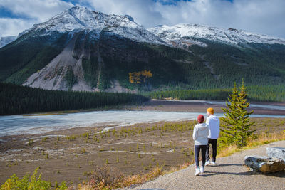 Rear view of people walking on snow covered mountains against sky