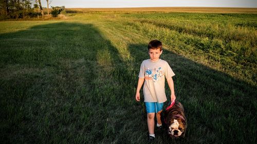 Full length of boy standing with dog on field