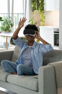 Happy excited young black woman enjoying virtual reality shopping experience while resting at home