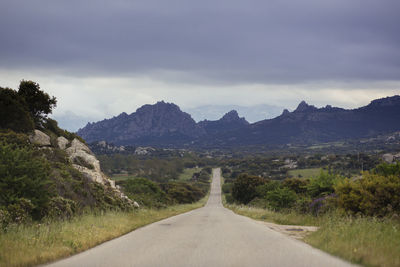 Empty road by mountains against cloudy sky