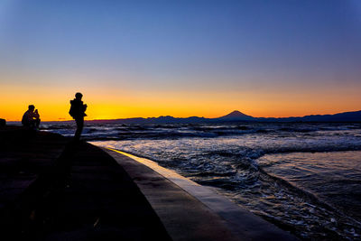 Rear view of man walking at the beach against clear sky during sunset