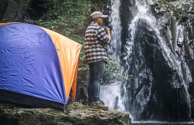 Male tourist standing and drinking coffee at the waterfall