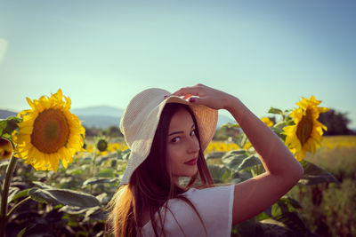 Portrait of young woman with sunflower against sky