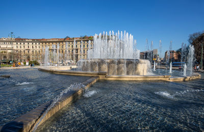 Fountain in city against clear blue sky