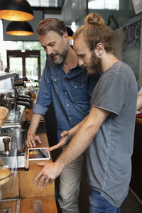 Coffee shop owner sharing tablet pc with barista in cafe