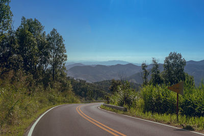 Empty road by trees against sky