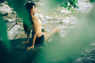 Side view of woman sitting on rocks at riverbank