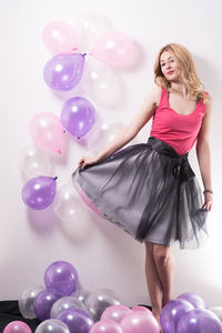 Portrait of beautiful young woman standing amidst balloons against wall