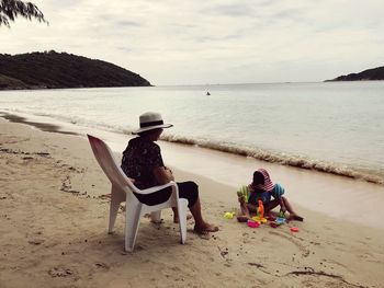 Rear view of people sitting on beach against sky