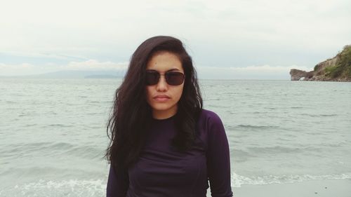 Portrait of young woman wearing sunglasses against sea at beach