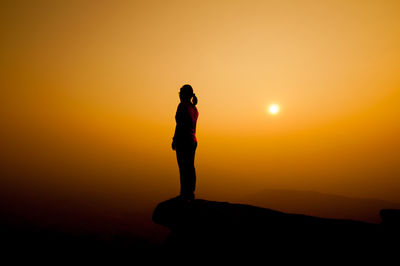 Silhouette woman standing on cliff against sky during sunset