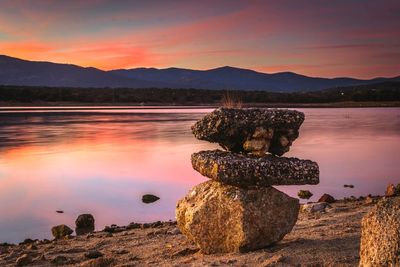 Stacked rocks by lake against sky during sunset