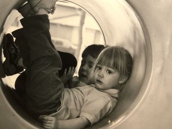 Full length of girl and boy sitting in playing equipment