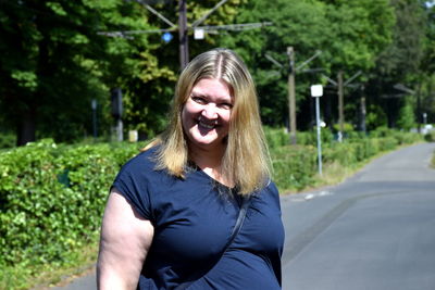 Portrait of smiling woman standing on road against trees