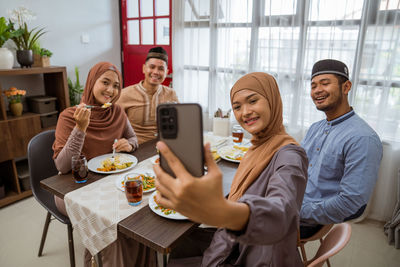 Smiling woman taking selfie while sitting at dining table
