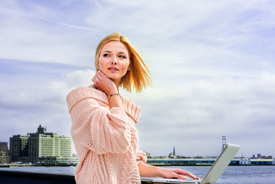 Young woman traveling in new york city, working on  laptop computer by river, looking, thinking.