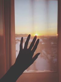 Close-up of hand against window during sunset