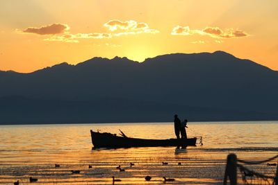 Silhouette man on boat at lake against sky during sunset