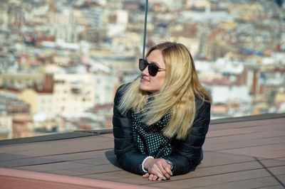 Young woman looking away while lying against cityscape