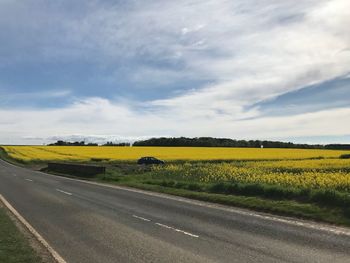 Scenic view of field by road against sky