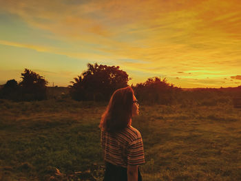 Rear view of woman standing on field against sky during sunset