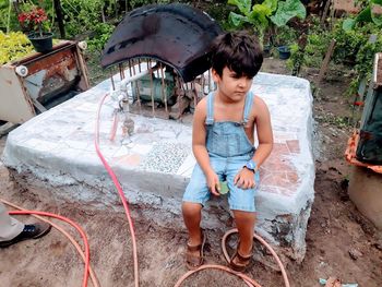 High angle view of boy sitting by water pump in yard
