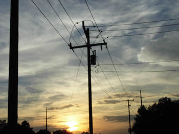 Low angle view of silhouette electricity pylon against cloudy sky