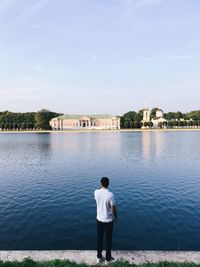 Rear view of man standing by lake against sky