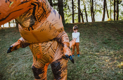 Boy playing with person wearing dinosaur costume in park