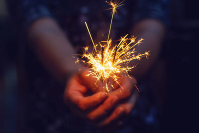 Midsection of person holding illuminated sparkler at night