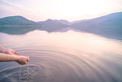 Cropped hand of man holding lake against sky during sunset