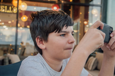 Portrait of young boy playing mobile phone games in a bar, with concentrated expression