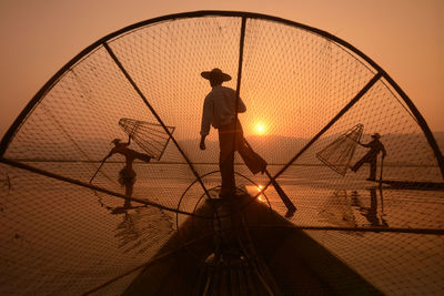 Fishermen on boats in lake against sky during sunset