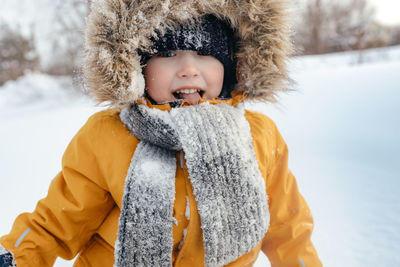 Smiling child in a fur hood in a knitted scarf and an orange winter jacket. outdoors. fashionable 