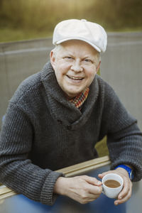 Portrait of happy man holding coffee cup while sitting at table outdoors