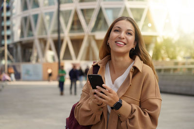 Portrait of smiling woman using mobile phone on street