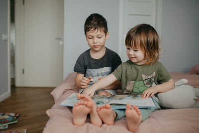 Older brother and younger sister reading in the bedroom on the bed. high quality photo