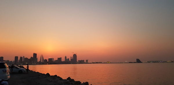 Scenic view of sea by buildings against sky during sunset