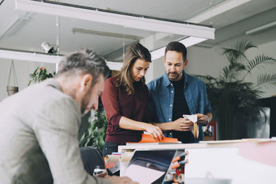 Businessman and businesswoman discussing while male colleague working on laptop in creative office