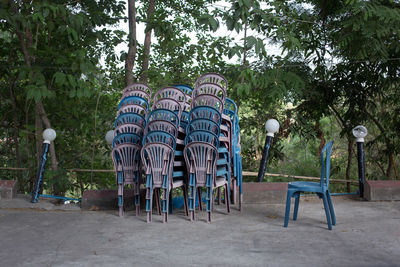 Stack of chairs on footpath against trees