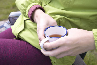 Female hands holding an iron mug with tea during a pause in training, a tourist at a halt